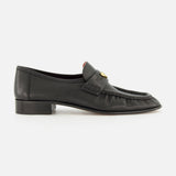 A pair of CHLOÉ Letti Gold Heart Loafers in black leather, featuring a low heel, moc toe stitching, and a signature gold-tone heart detail on the top—these feminine flats are pictured from the side against a white background, exemplifying the timeless elegance of classic Chloé design.