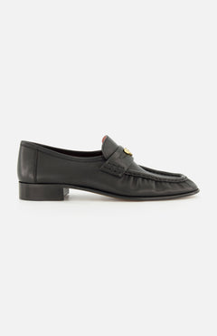 A pair of CHLOÉ Letti Gold Heart Loafers in black leather, featuring a low heel, moc toe stitching, and a signature gold-tone heart detail on the top—these feminine flats are pictured from the side against a white background, exemplifying the timeless elegance of classic Chloé design.