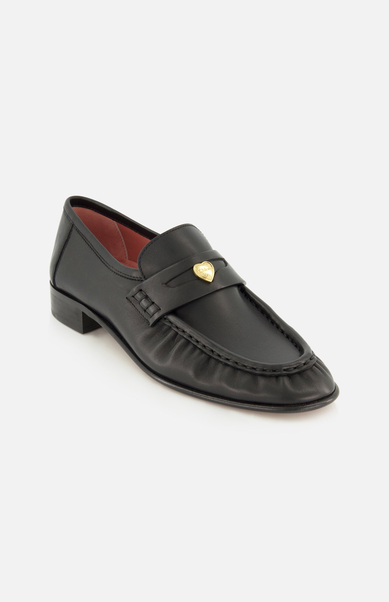 The Letti Gold Heart Loafers by CHLOÉ feature black leather construction with a gold heart-shaped embellishment on the strap, a low heel, and striking red interior lining. Displayed against a white background, these flats blend classic style with playful elegance, making them the perfect feminine choice for any occasion.