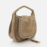 The CHLOÉ Marcie Suede Top Handle Bag, shown in taupe with a curved flap, gold hardware, thick leather handles, visible stitching, and a decorative strap with gold accents, is displayed against a white background.