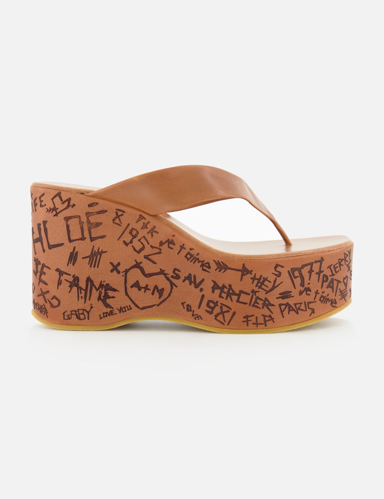 The Maxime Wedged Thong Sandals by CHLOÉ feature a brown wedge with a wood-effect platform decorated in black graffiti-style writing and symbols, complemented by a brown leather thong strap, shown against a white background.
