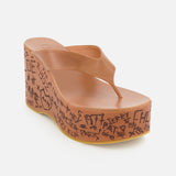 The Maxime Wedged Thong Sandals by CHLOÉ showcase brown leather straps and a thick, wood-effect platform wedge sole adorned with doodle-like black text and symbols along the side. Set against a plain white background.