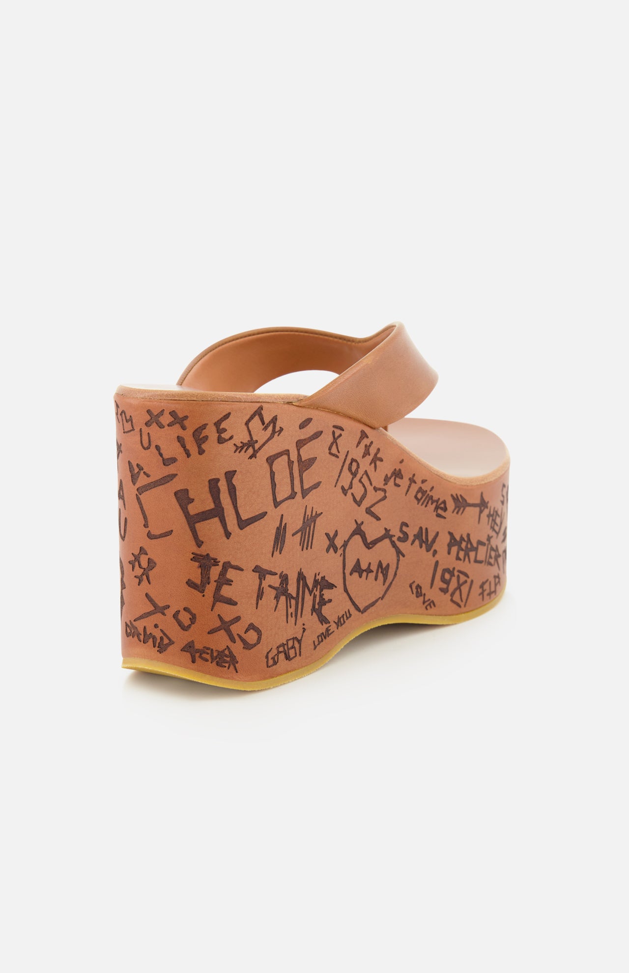 The Maxime Wedged Thong Sandals by CHLOÉ are tan platform sandals featuring an open toe and decorated with graffiti-style black doodles and the word “CHLOE” along the outer side of their wood-effect platform and heel.