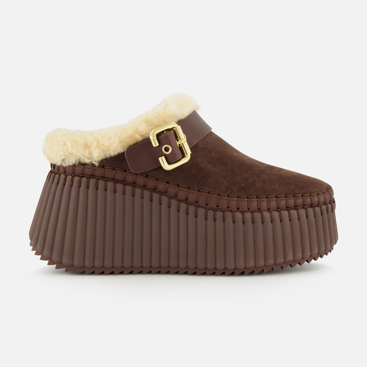 Introducing the Nama Suede Slippers by CHLOÉ—these brown suede platform mules feature a chunky, ridged rubber sole, plush cream shearling lining, and an elegant gold buckle detail at the side. Designed for both comfort and effortless style, these slip-ons are the perfect cozy addition to your wardrobe.