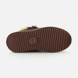 The image displays the ridged brown rubber sole of CHLOÉ’s Nama Suede Slippers, featuring the brand’s circular logo embossed at the center. A glimpse of the upper reveals soft light fur and a sleek strap, reflecting its plush shearling lining. This platform slip-on design effortlessly merges comfort and luxurious style.