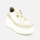 The CHLOÉ Nama Charm Detail Sneaker is a white shoe with a thick recycled sole, olive green accents, tan stitching, gold and orange lace charms, and a light blue heel detail, shown on a plain white background.