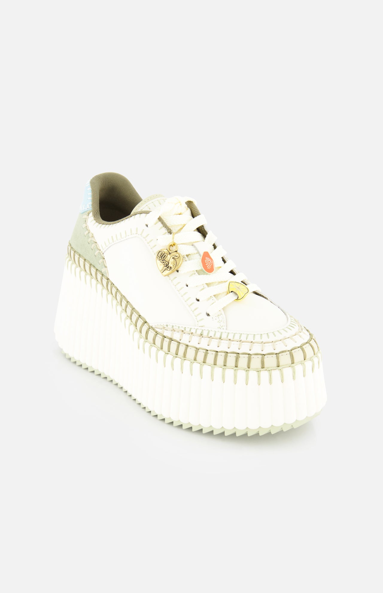The CHLOÉ Nama Charm Detail Sneaker is a white shoe with a thick recycled sole, olive green accents, tan stitching, gold and orange lace charms, and a light blue heel detail, shown on a plain white background.