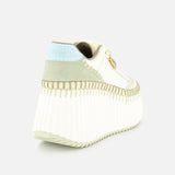 The Nama Charm Detail Sneaker by CHLOÉ features white leather, a recycled wedge sole, ribbed chunky design, pale green and blue suede accents, a gold logo charm, and detailed stitching—shown from the back-left against a white background.