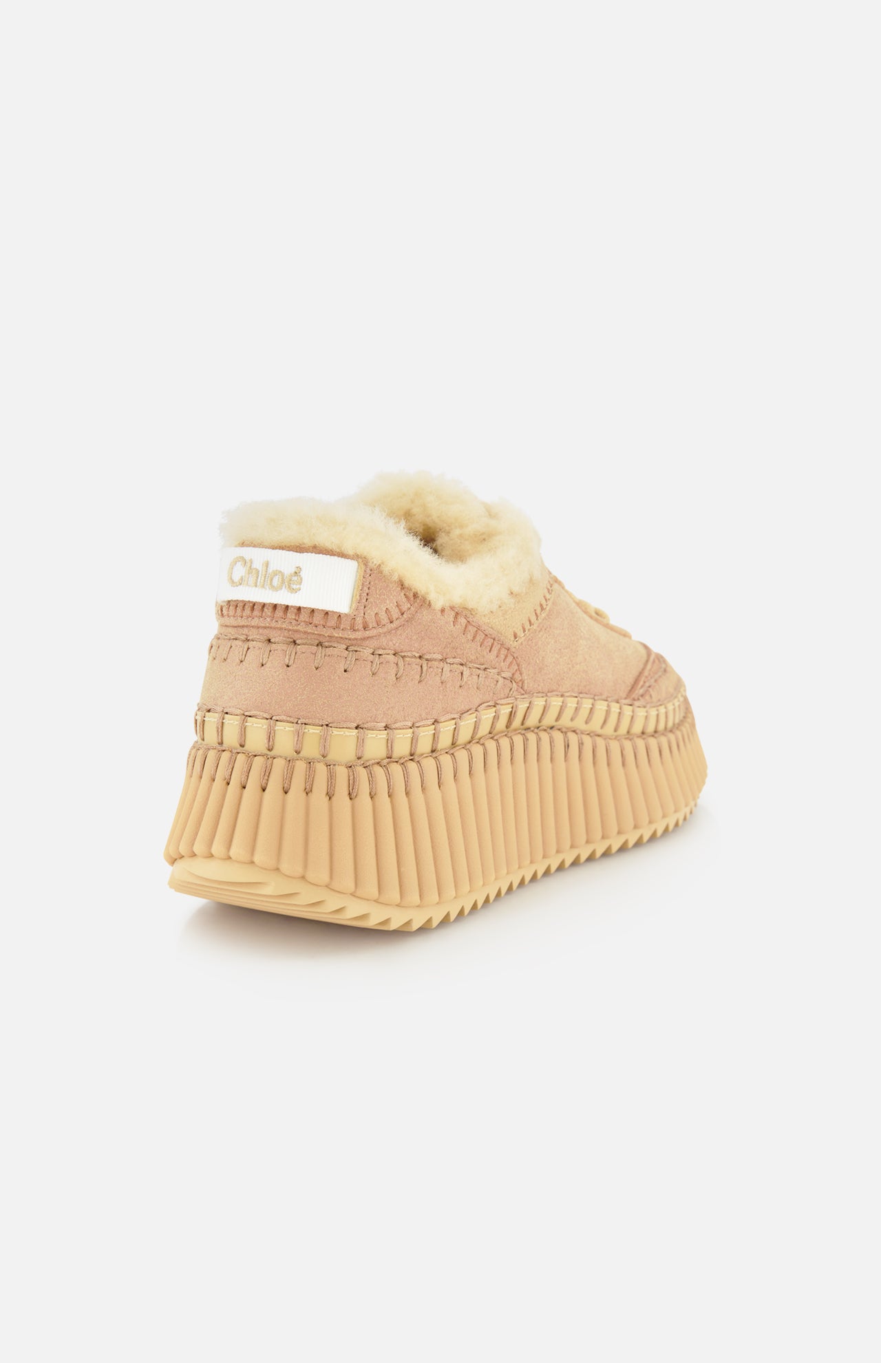 The Nama Shearling Lining Sneakers by CHLOÉ are beige slip-on shoes featuring a thick, ribbed recycled sole, visible stitching, and cream-colored shearling lining. Chloé branding appears on a white label at the heel.