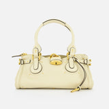 The CHLOÉ Paddington Shoulder Bag in cream grained buffalo leather features gold hardware, circular handles, a central oversized padlock, and a zipper pull detail, shown against a white background.
