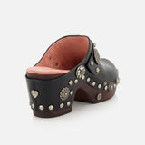 CHLOÉ Talis Studded Leather Clogs in black leather with a wooden platform heel, accented with decorative silver-tone studs in various floral and circular shapes, including a heart-shaped stud on the heel.