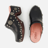CHLOÉ Talis Studded Leather Clogs in black with wooden soles and decorative silver-tone studs, shown from the side and top in a slip-on design.