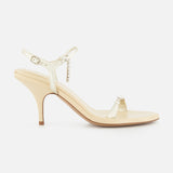 The Zia Crystal Chain Heels by CHLOÉ are elegant beige heeled sandals featuring a slim ankle strap with a delicate buckle and an open toe, crafted in the refined style of classic Italian designer shoes and displayed in profile against a plain white background.