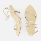 A pair of Zia Crystal Chain Heels by CHLOÉ, featuring beige high heels with slender straps—one accentuated by a sparkling crystal chain—for an elegant interpretation of Italian designer footwear. Displayed on a white background, one shoe is shown from the top and the other from the side.