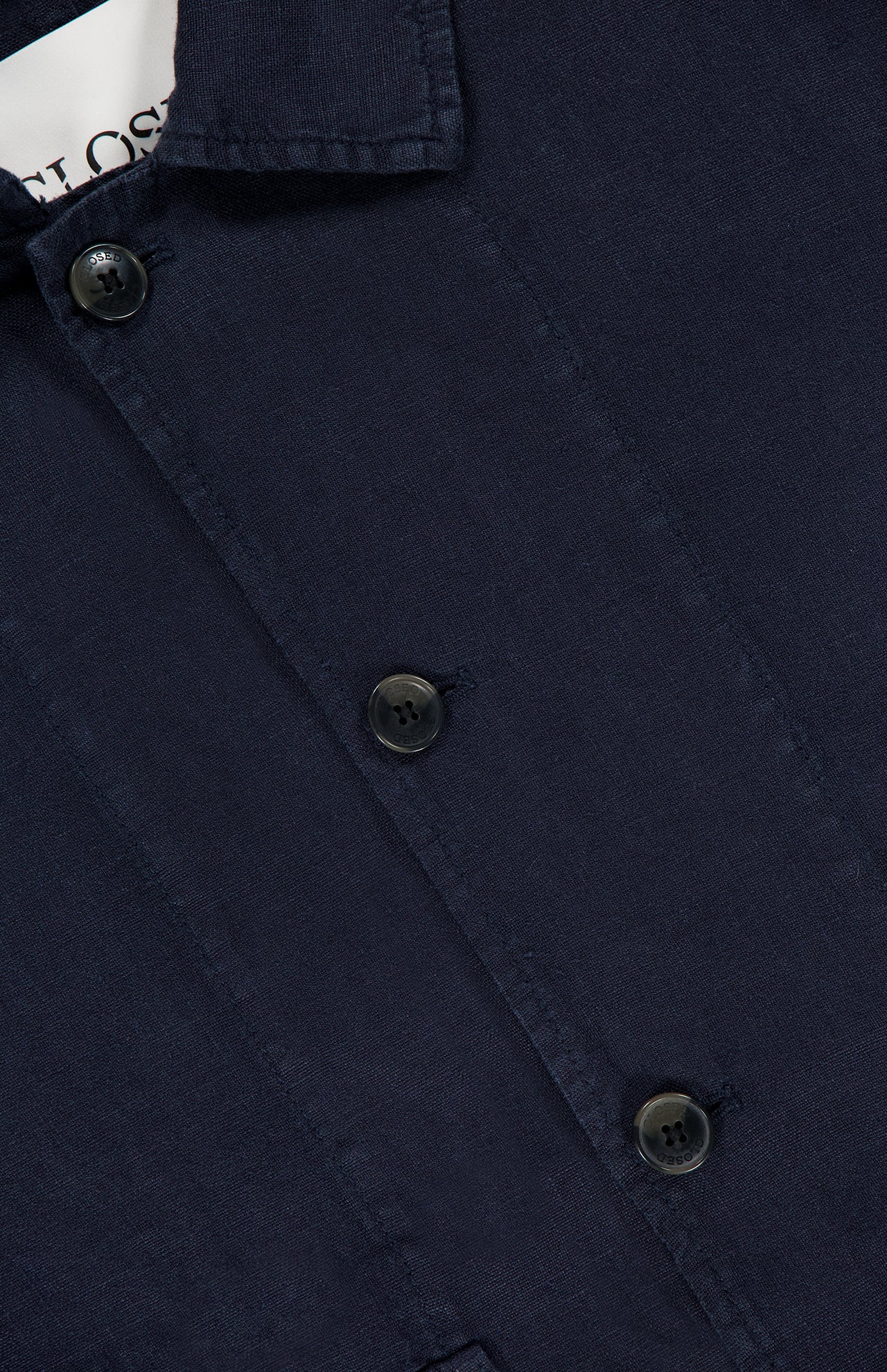 Close-up of a navy blue button-up shirt with three dark buttons and a hint of a white tag—ideal for pairing with the CLOSED Linen Cargo Jacket, thanks to its classic button-front design.