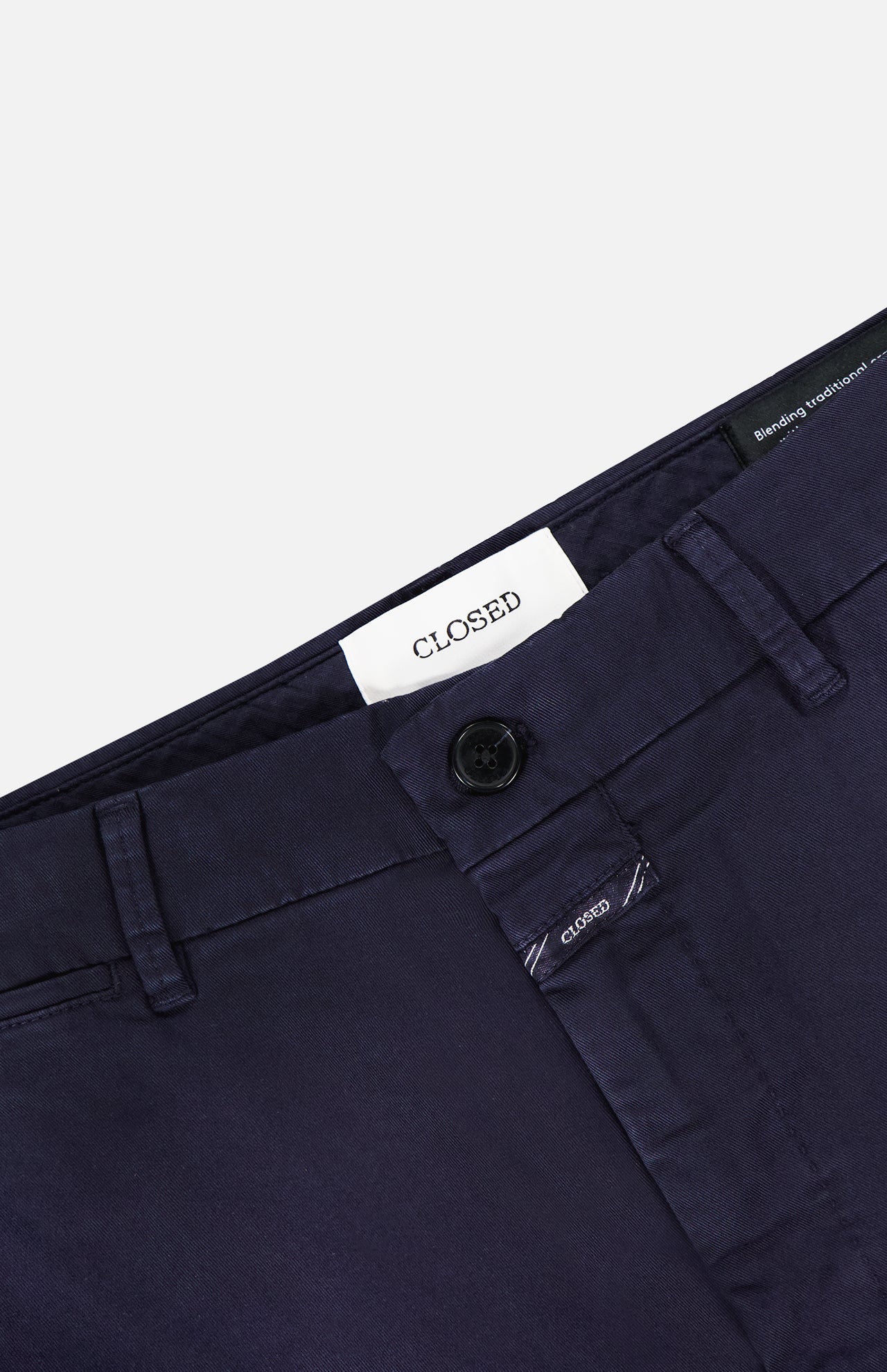 Close-up of the waistband of Classic Chino Shorts by CLOSED, made from dark navy stretch cotton twill with belt loops, a button closure, and an inner white label reading CLOSED. The smooth fabric has a slight sheen.