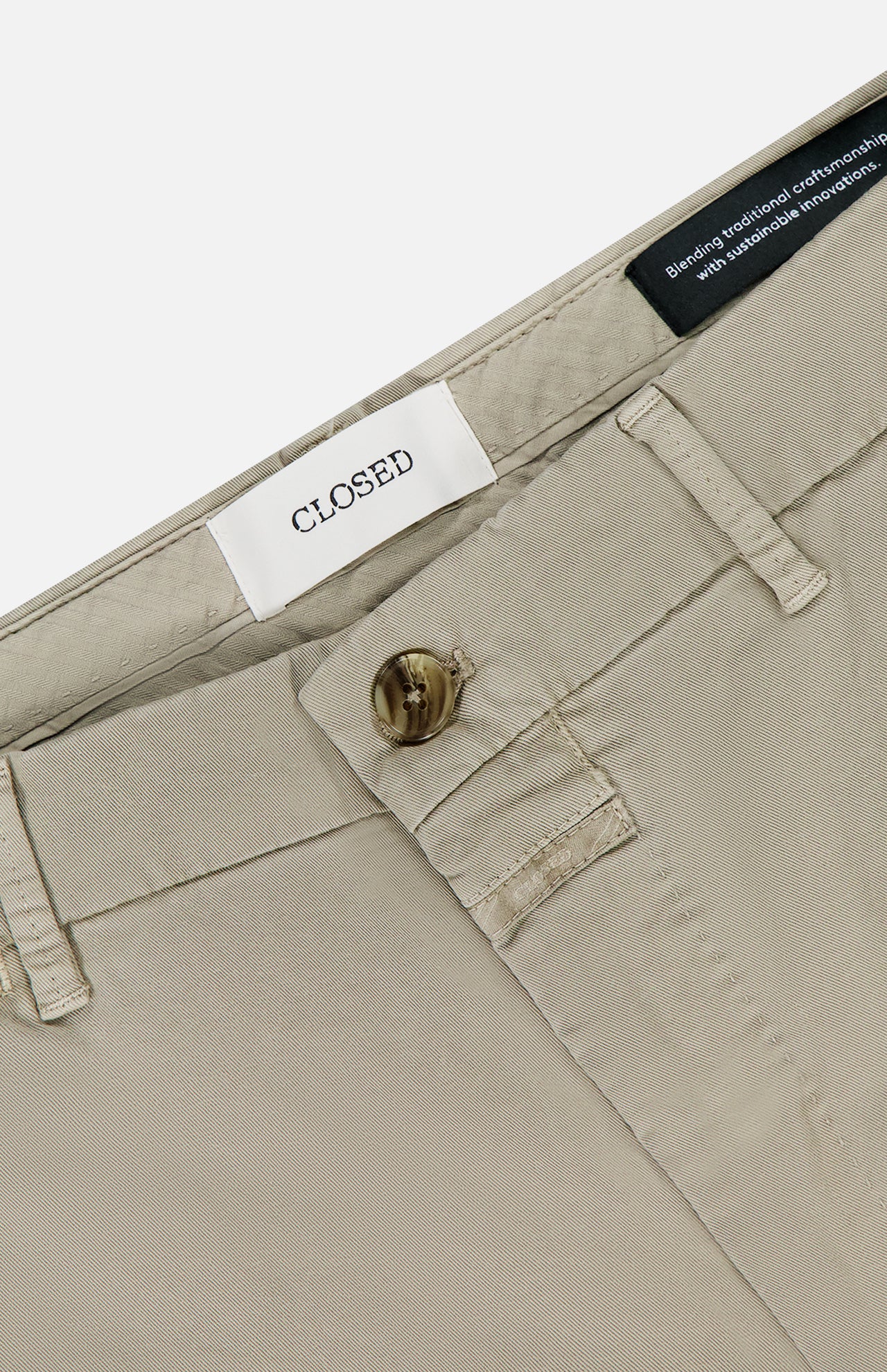 Close-up of Classic Chino Shorts by CLOSED in stretch cotton twill, featuring a button closure, belt loops, and a white brand label sewn inside the waistband with part of a black inner label also visible.