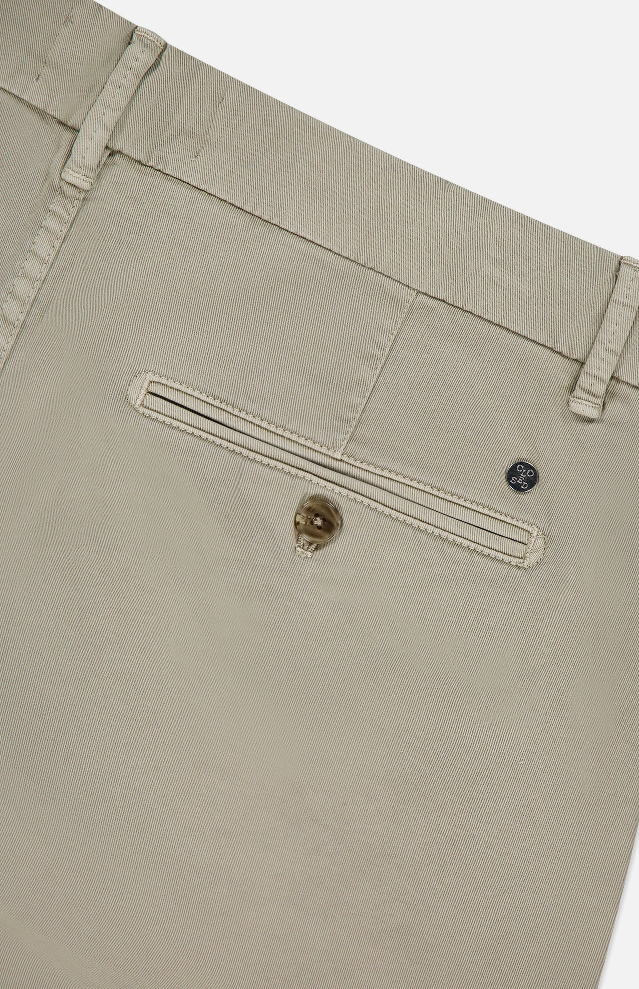 Close-up of the back pocket of CLOSED Classic Chino Shorts in beige stretch cotton twill, featuring a button closure, visible belt loops, and a small metal tag above the pocket.
