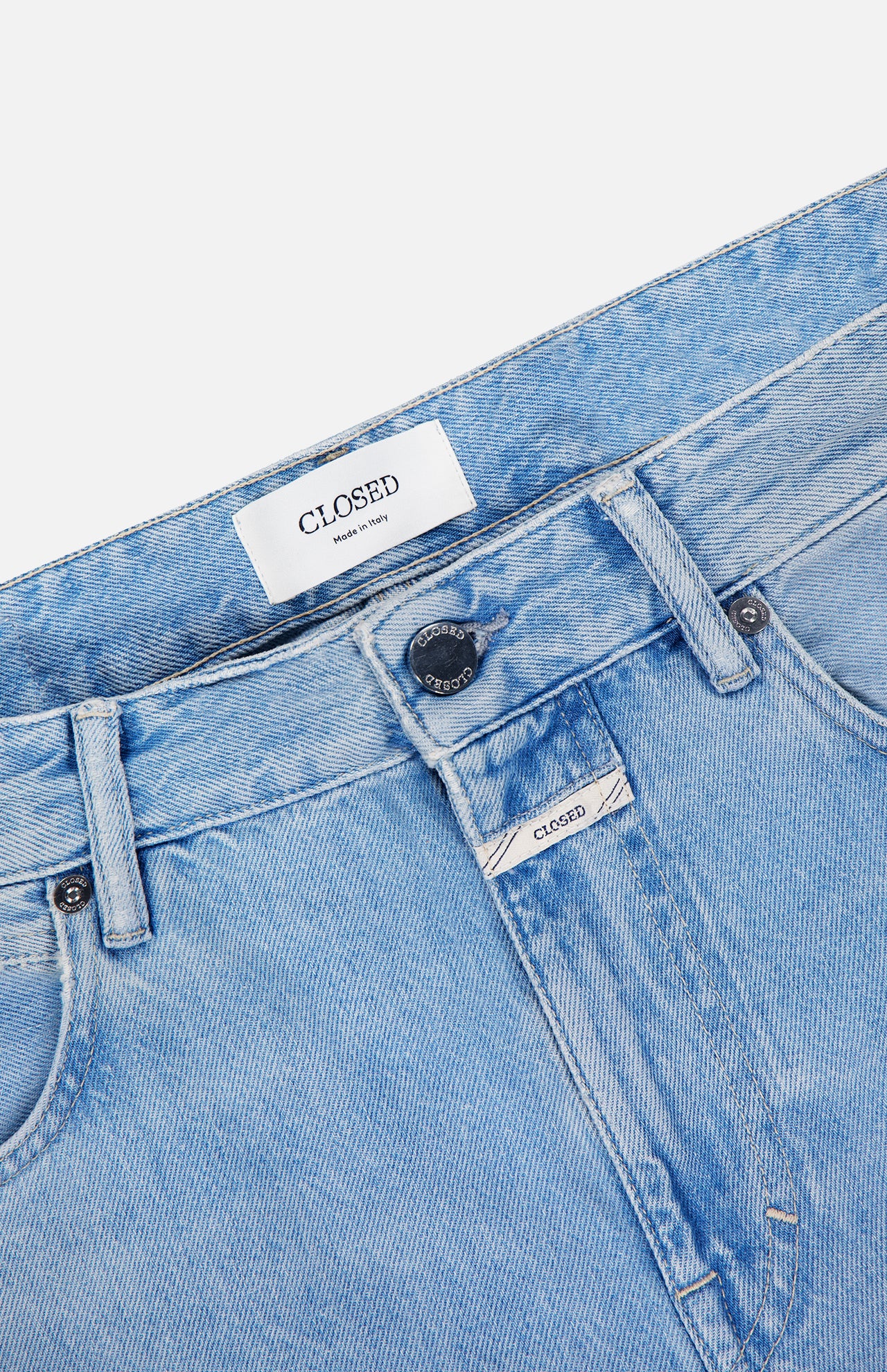 Close-up of the waistband and top front of the Cooper True Straight Leg Denim jeans in light blue by CLOSED, featuring a branded label, button, belt loops, and part of the front pockets against a white background. Crafted from sustainable denim and made in Italy.