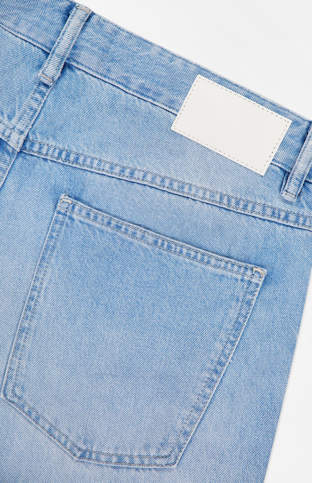Close-up of the back pocket and waistband of light blue Cooper True Straight Leg Denim jeans by CLOSED, with a blank white label above the pocket. The fabric texture and stitching details are clearly visible, highlighting the high-quality craftsmanship characteristic of these Italian-made sustainable jeans.