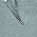 A close-up of the HALF ZIP JUMPER SWEATER by CLOSED in light teal cotton-blend fabric, featuring a partially unzipped silver zipper and a white label with the brand name CLOSED.