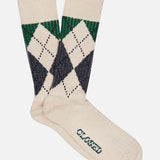 A pair of CLOSED Argyle Socks in a cream color, featuring a green and navy argyle pattern near the top and the word “CLOSED” printed in green on the sole.