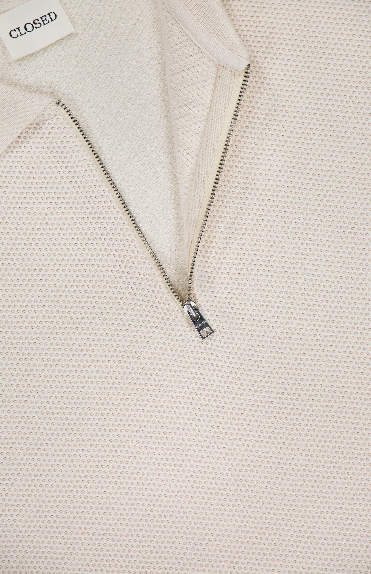 Close-up of the Zipped Neck Polo Shirt by CLOSED, crafted from textured cream cotton with a partially open silver half-zip and a white CLOSED label at the collar.