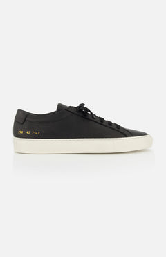 The COMMON PROJECTS Achilles Premium Grained Leather Sneaker is shown in profile, featuring black leather, black laces, a white rubber sole, and gold numbers on the heel against a plain white background.