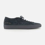 The COMMON PROJECTS Achilles Suede Premium Sneakers in dark navy feature a minimalist design with black laces, a gray rubber sole, and gold numbers stamped on the heel, displayed in a side profile view against a white background.