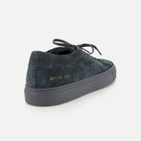 The COMMON PROJECTS Achilles Suede Premium Sneakers are luxury low-top navy suede sneakers featuring laces, a gray rubber sole, and gold numbers 2611 43 4298 on the heel, shown against a plain white background.