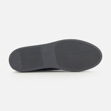 The image displays the bottom view of the COMMON PROJECTS Achilles Suede Premium Sneakers in dark gray, featuring a minimalist sole design with a textured, non-slip pattern and a rectangular section with horizontal lines at one end.