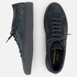 A pair of COMMON PROJECTS Achilles Suede Premium Sneakers in dark green suede features black soles and laces, shown from the side and top. The insoles are stamped with “COMMON PROJECTS” and “MADE IN ITALY” in gold lettering, emphasizing their luxurious low-top design.