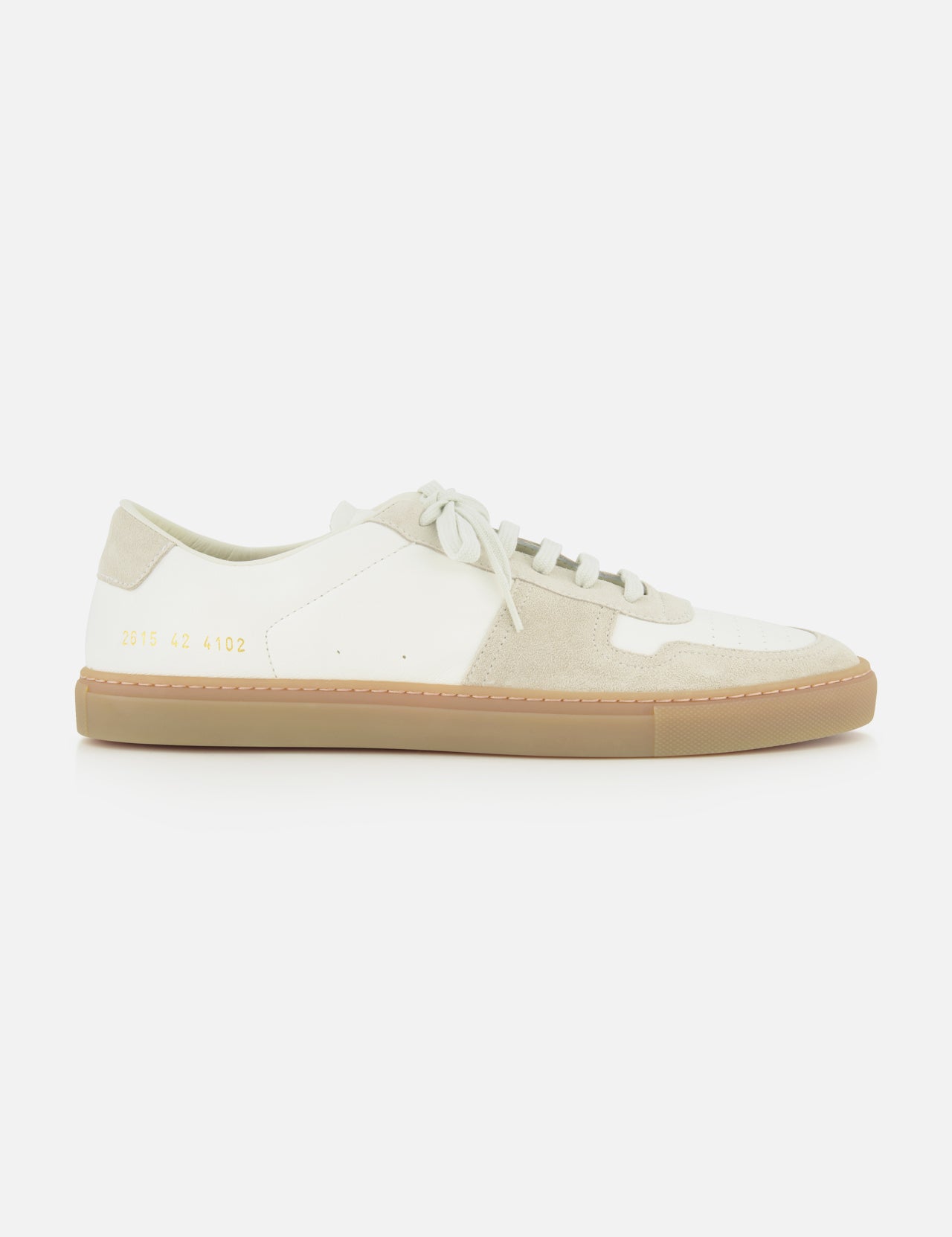 The Bball Duo Leather and Suede Sneaker by COMMON PROJECTS is a luxury low-top shoe crafted from off-white leather with beige suede panels, featuring white laces, a beige rubber sole, and gold numbers printed near the heel on the outer side.