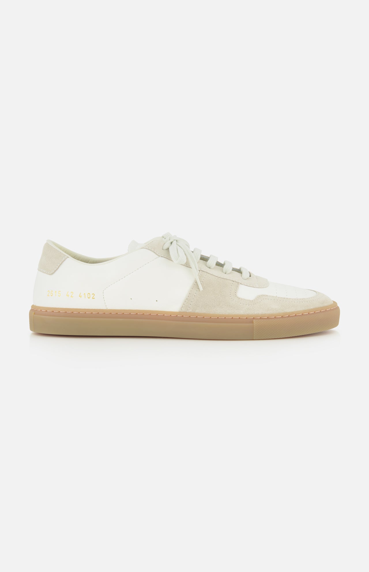The Bball Duo Leather and Suede Sneaker by COMMON PROJECTS is a luxury low-top shoe crafted from off-white leather with beige suede panels, featuring white laces, a beige rubber sole, and gold numbers printed near the heel on the outer side.