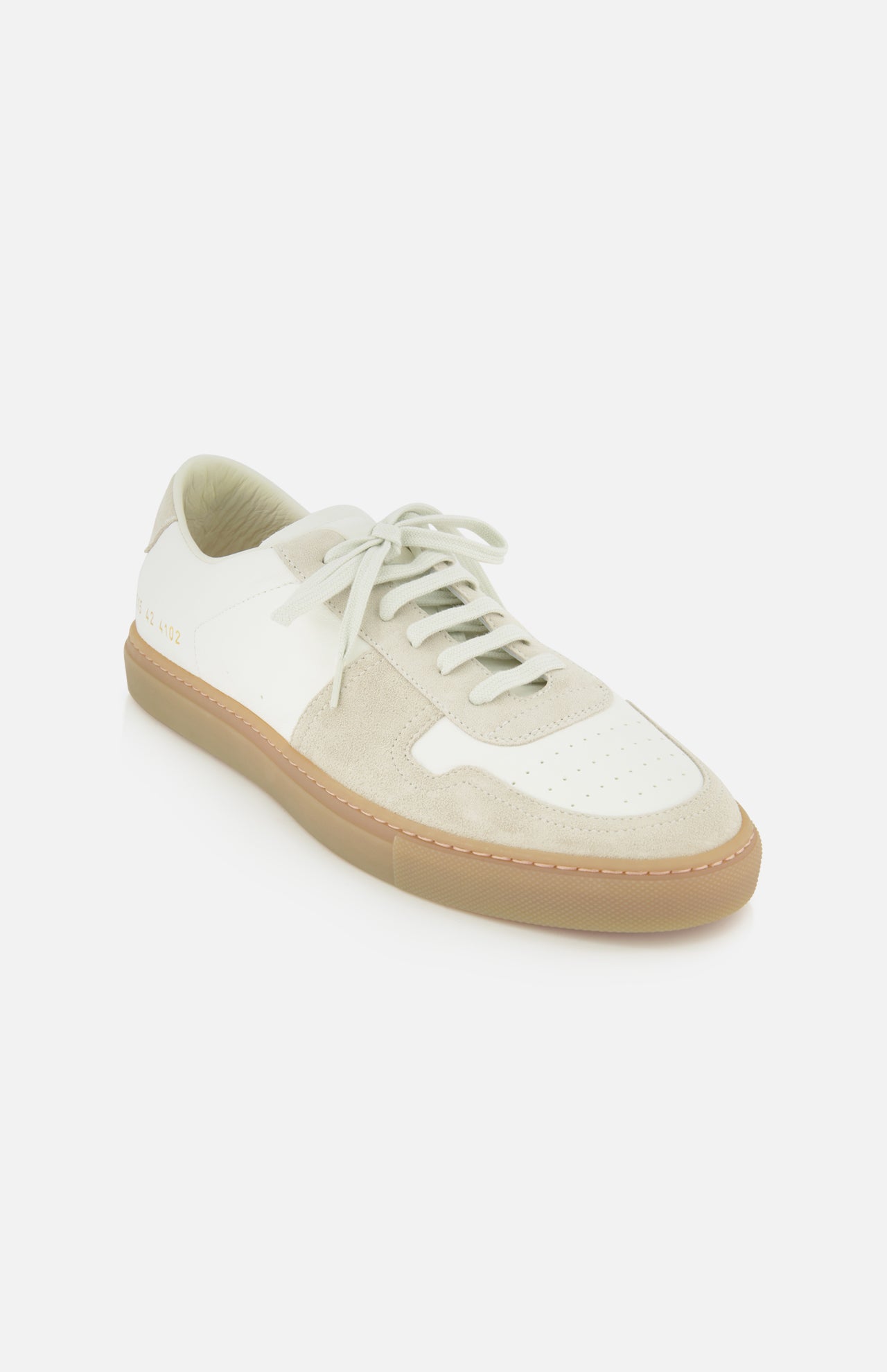 The COMMON PROJECTS Bball Duo Leather and Suede Sneaker is a luxury low-top shoe in white and beige, featuring premium suede and off-white leather panels, white laces, and a tan rubber sole, showcased against a plain white background.