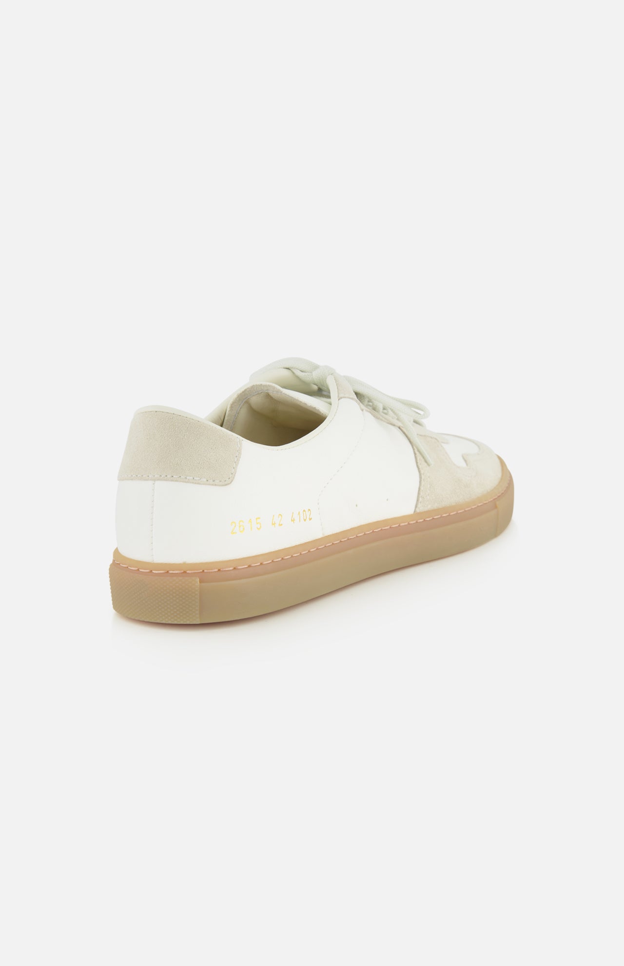 The COMMON PROJECTS Bball Duo Leather and Suede Sneaker is displayed from a rear angle against a white background, highlighting its white and beige design with a gum sole. Signature gold numbers are stamped near the heel, emphasizing the refined details of this luxury low-top shoe.