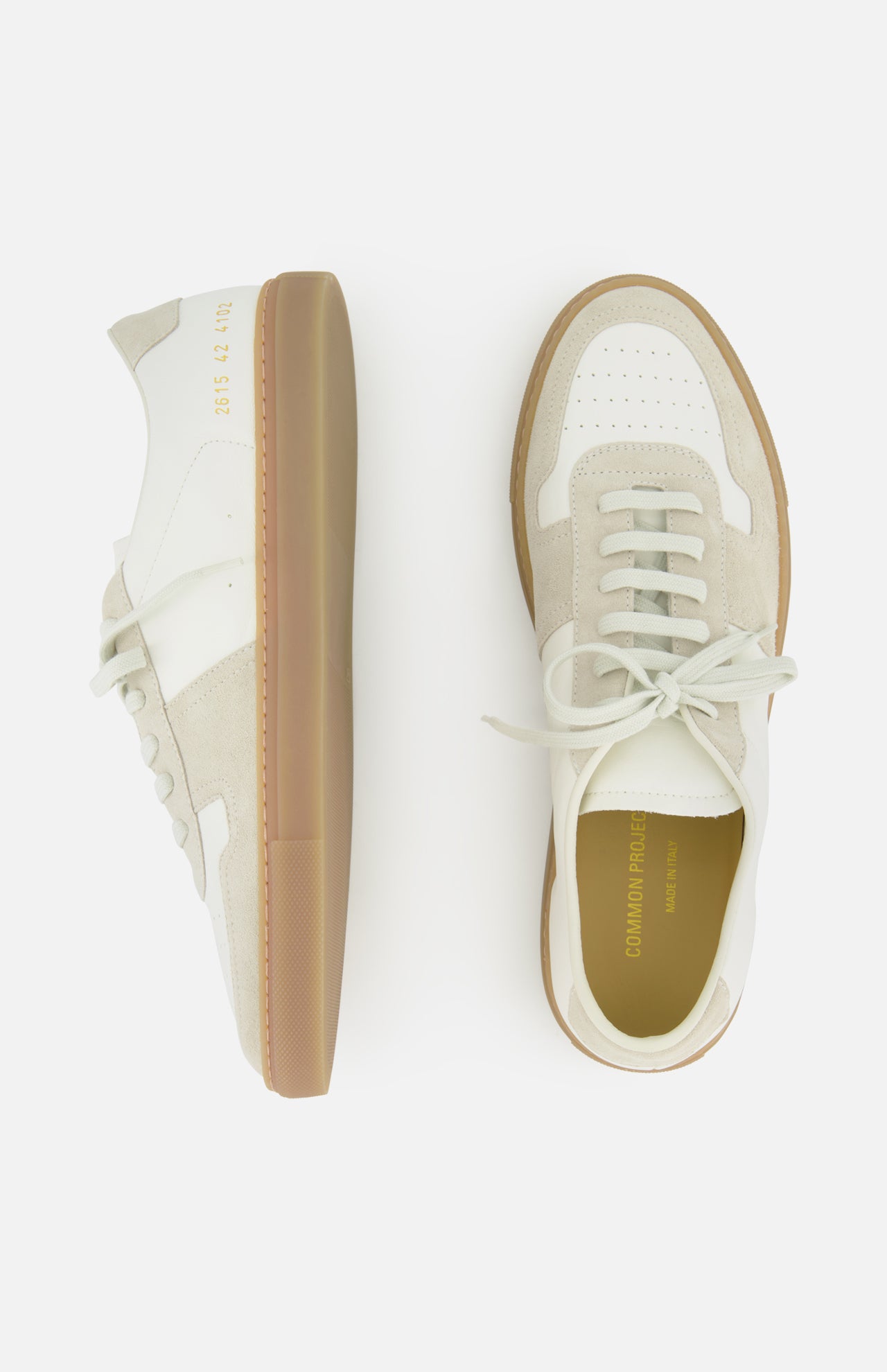 A pair of COMMON PROJECTS Bball Duo Leather and Suede Sneakers in white and beige, featuring gum soles. One off-white leather sneaker is displayed from the side, while the other is shown from above, highlighting the laces and a gold-stamped brand name on the insole. Set against a white background.