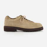 The Hiker Low Suede Piuma Boot by COMMON PROJECTS features a beige suede upper, lace-up closure, a low-profile dark brown sole, visible stitching, and a minimalist design. Shown in a side view against a white background.