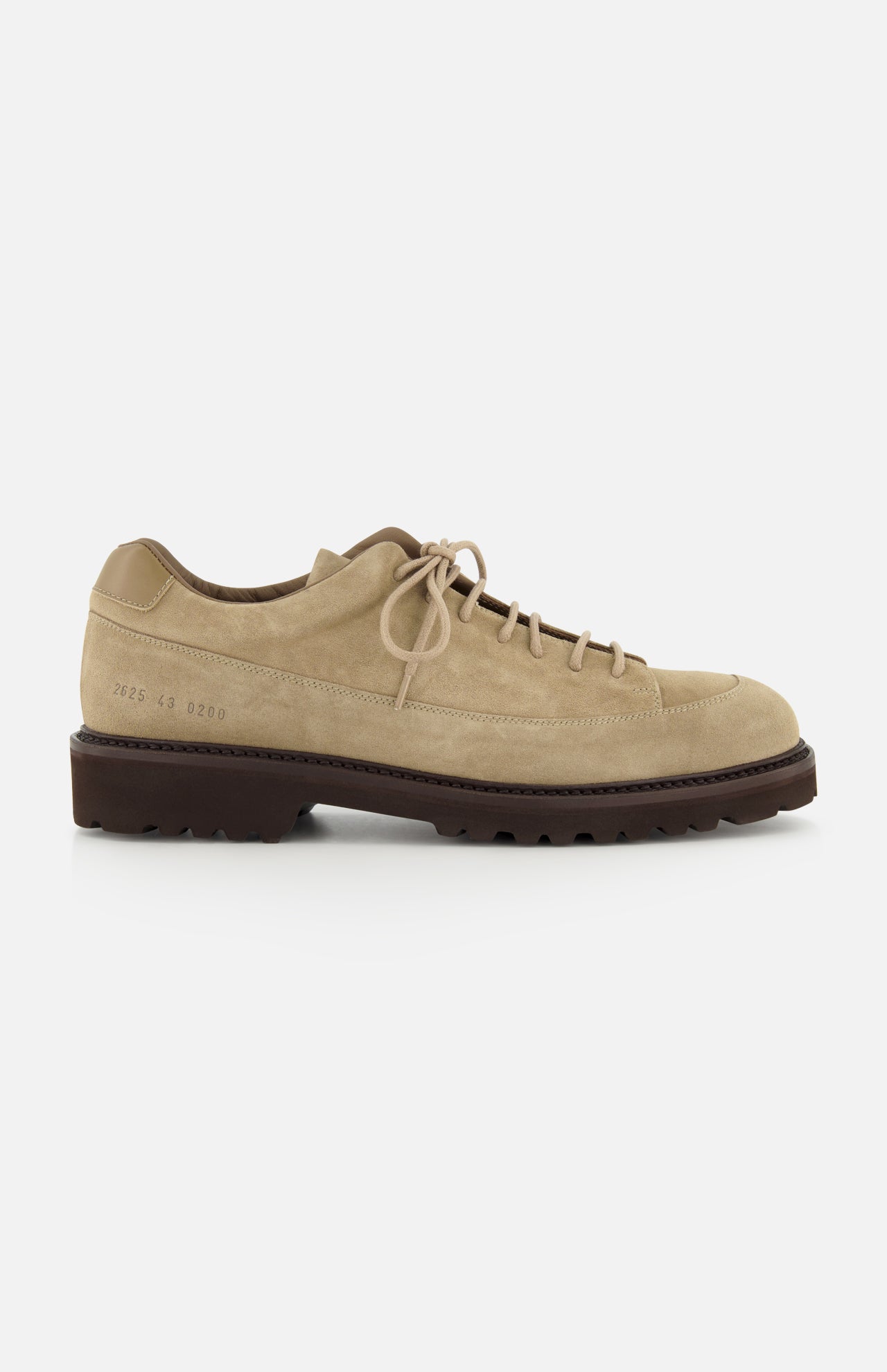 The Hiker Low Suede Piuma Boot by COMMON PROJECTS features a beige suede upper, lace-up closure, a low-profile dark brown sole, visible stitching, and a minimalist design. Shown in a side view against a white background.