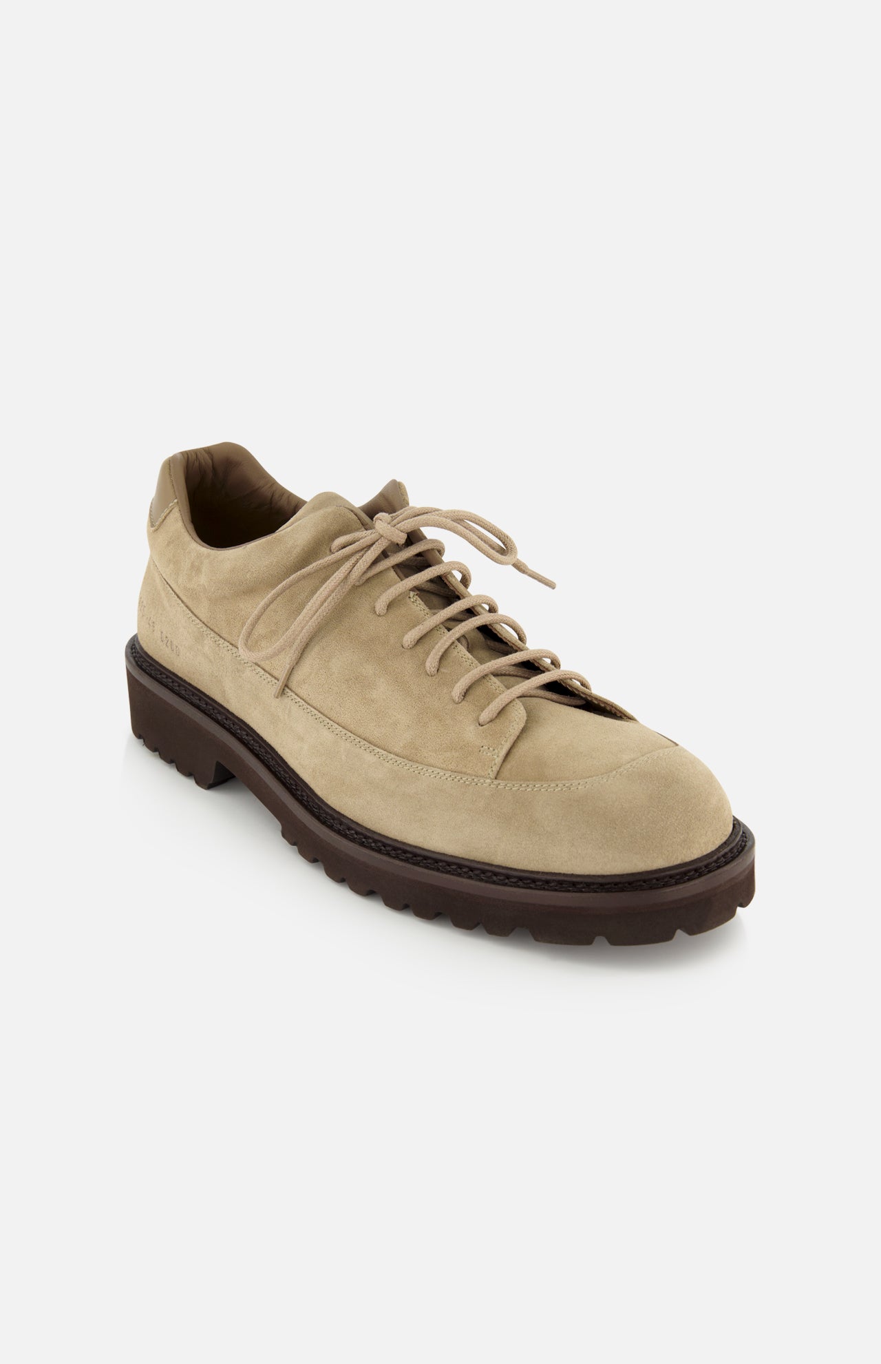 The COMMON PROJECTS Hiker Low Suede Piuma Boot is shown in beige suede with a dark brown, rugged textured sole and visible stitching, viewed from the front left angle on a white background.