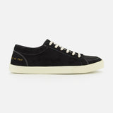 The COMMON PROJECTS Premium Skate In Nubuck Sneaker is a black nubuck low-top with white laces and a crisp white sole, displayed from the side. Signature gold numbers stamped near the heel lend an exclusive touch to this luxury designer shoe, while visible white stitching highlights its refined construction.