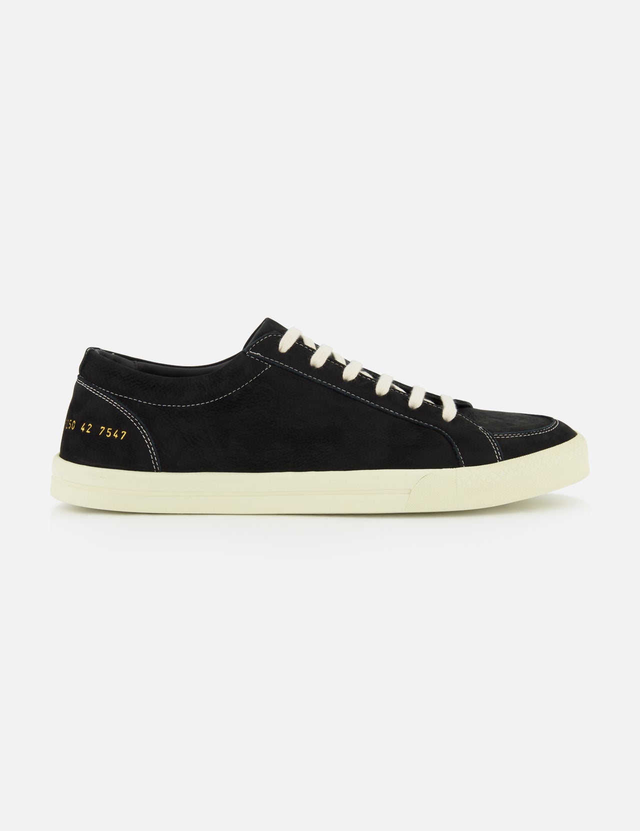 The COMMON PROJECTS Premium Skate In Nubuck Sneaker is a black nubuck low-top with white laces and a crisp white sole, displayed from the side. Signature gold numbers stamped near the heel lend an exclusive touch to this luxury designer shoe, while visible white stitching highlights its refined construction.