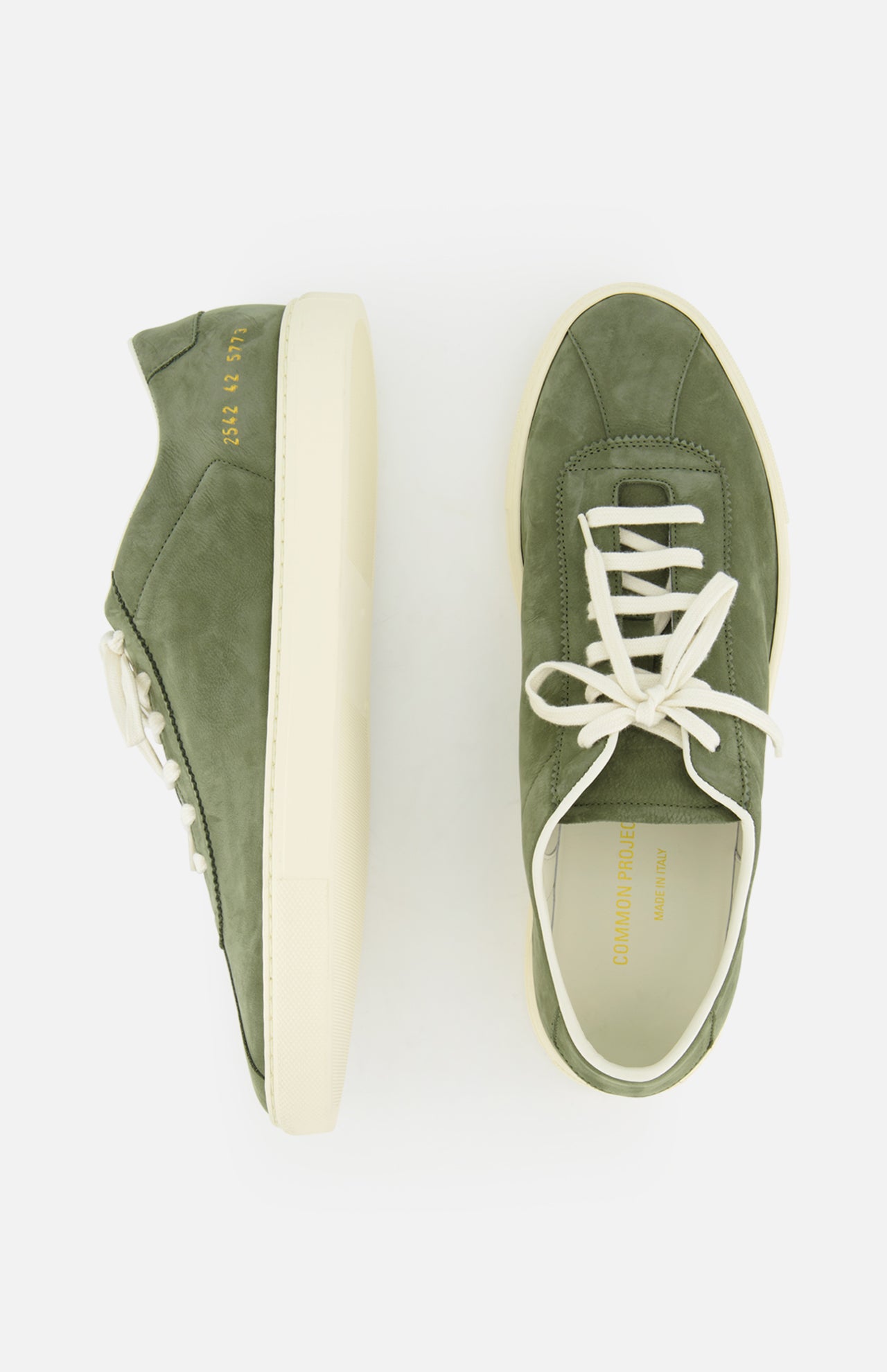 The Leather Tennis Sneaker by COMMON PROJECTS is an olive green suede luxury street shoe with white laces, cream rubber soles, and gold embossed branding on the side and insole. Shown from side and top view on a white background.