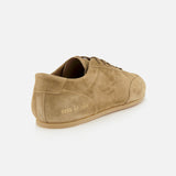 The COMMON PROJECTS Winter Suede Driving Sneaker is shown from the back, featuring tan suede construction in a taupe shade with a gum sole. Distinct gold numbers are stamped near the heel for a refined accent. This luxury low-top showcases visible stitching and laces in a minimalist design.
