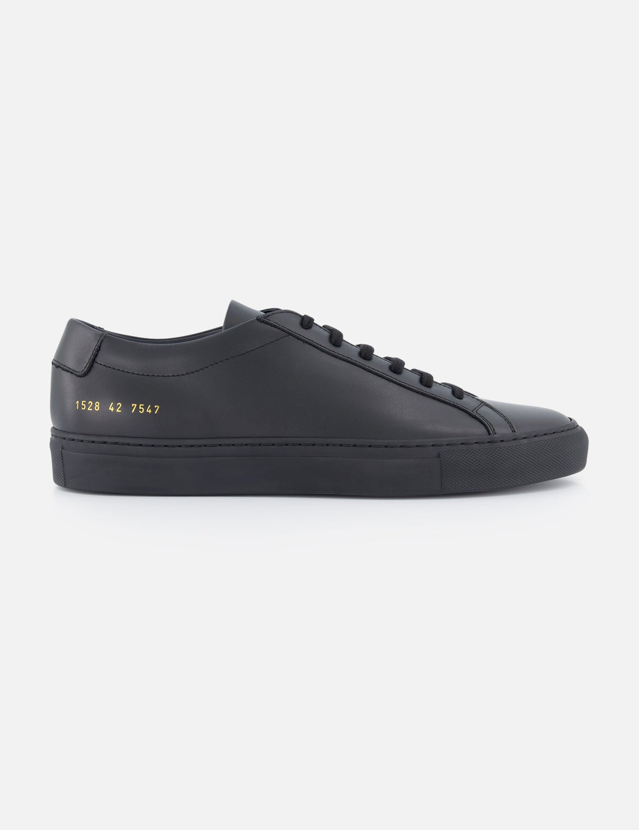 The COMMON PROJECTS Men's Original Achilles Low Sneaker in black leather features a minimalist low-top design with black laces, a flat sole, and gold numbers stamped on the heel’s side, shown on a white background from the side view.