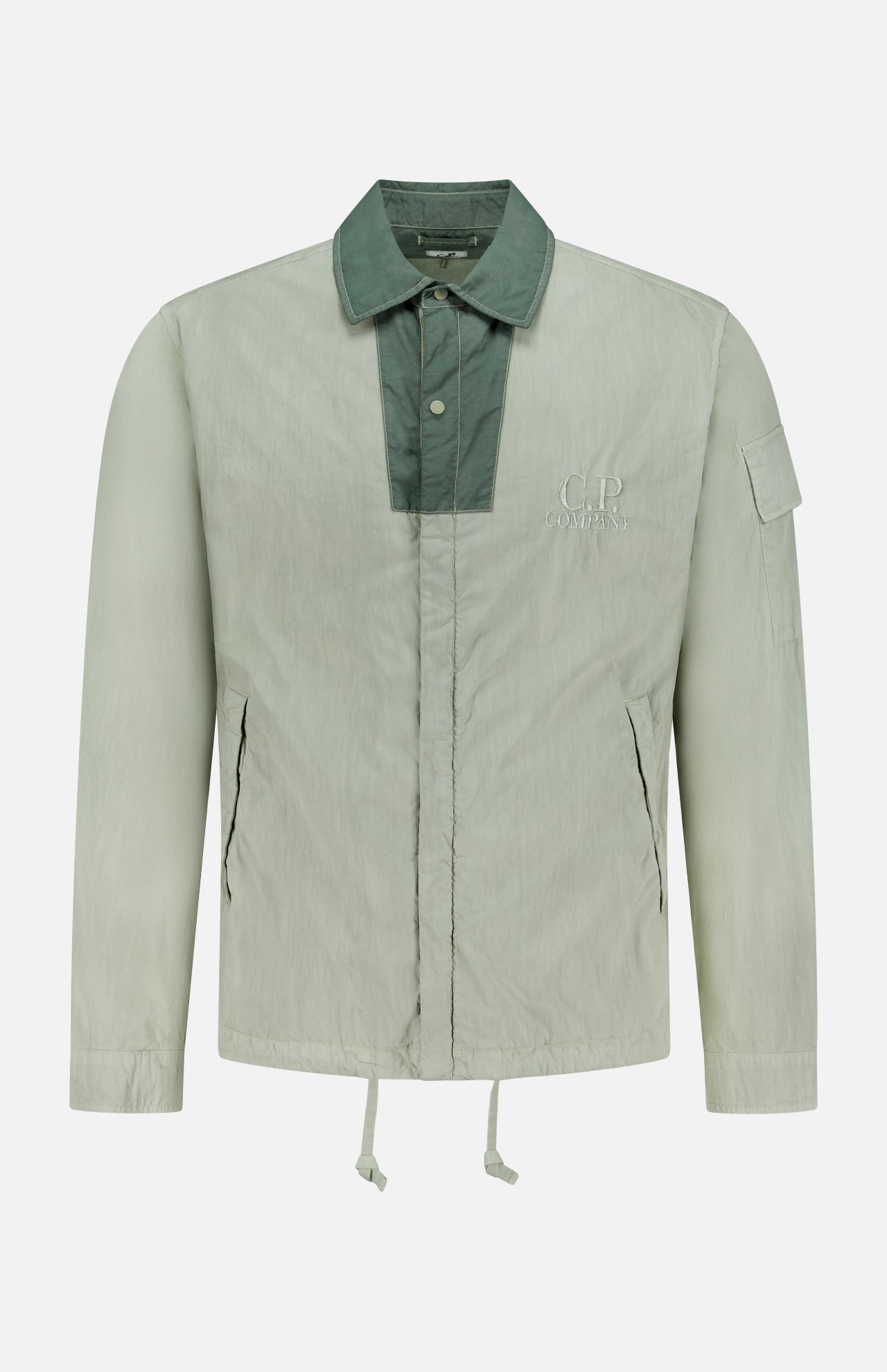 The C.P. COMPANY 50 Fili Two-tone Overshirt is a light gray-green technical overshirt with a dark green collar and chest placket, zippered front pockets, a sleeve pocket, chest logo, relaxed fit, and drawstring hem for utilitarian style.