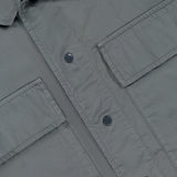 Close-up of the Cotton Rip-Stop Overshirt by C.P. COMPANY in grey, showcasing two large front pockets, metal snap buttons, and smooth 100% cotton fabric with a visible white label at the top left.