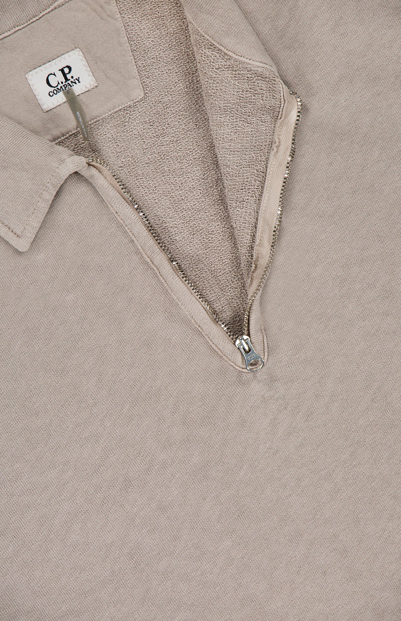 Close-up of the Malfile Fleece Polo Collar Sweatshirt by C.P. COMPANY in beige, featuring a partially open silver zip and textured inner fabric. A white label inside the collar showcases refined designer sportswear details.