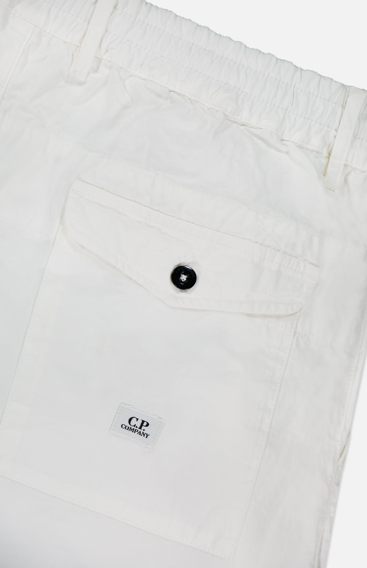 Close-up of C.P. COMPANY Micro-Reps Boxy Loose Pants in white, made from high-density cotton with an elastic waistband, large flap back pocket with black button, and small C.P. Company logo label below the pocket.