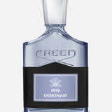 A clear glass Creed Iris Debonair 100 ml Fragrance bottle with a metallic cap, featuring a black leather wrap around the lower half and an Iris Debonair label.